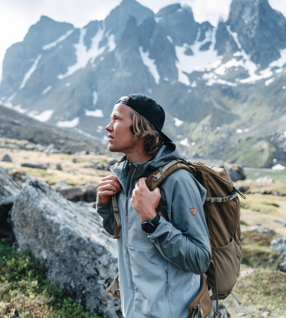 Mann med caps og sekk ser opp mot fjellene. Foto.