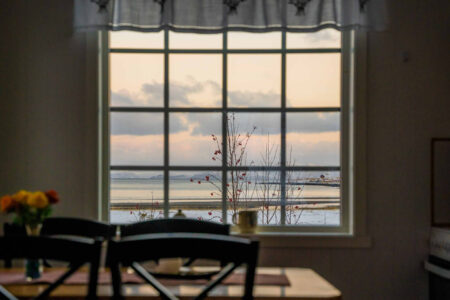 Utsikt fra vindu med sprosser mot hav i snødekt landskap. Foto.