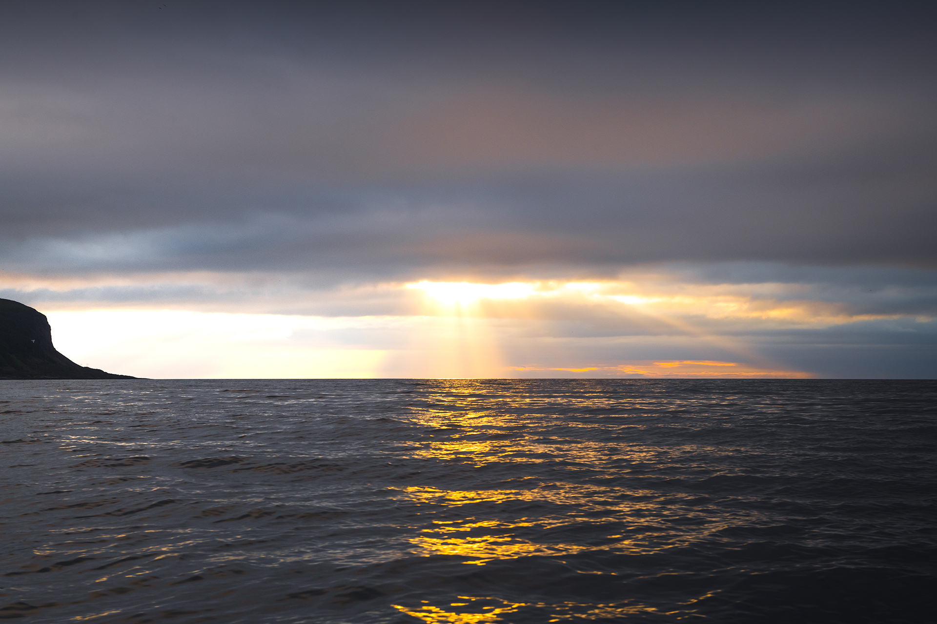 Sol skinner gjennom skyer over havet. Foto.