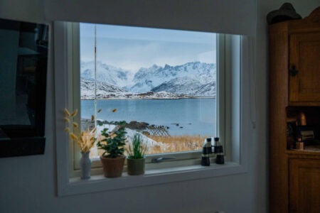 Utsikt fra stue ut mot sjø og snødekte fjell. Foto.