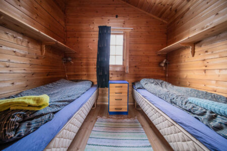 Soverom med to senger på hver sin kant av rommet. Foto.