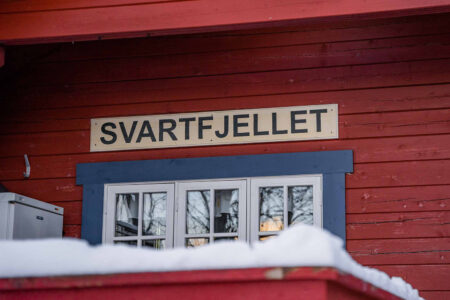 Rød hyttevegg med vindu og skilt med "SVARTFJELLET". Foto.
